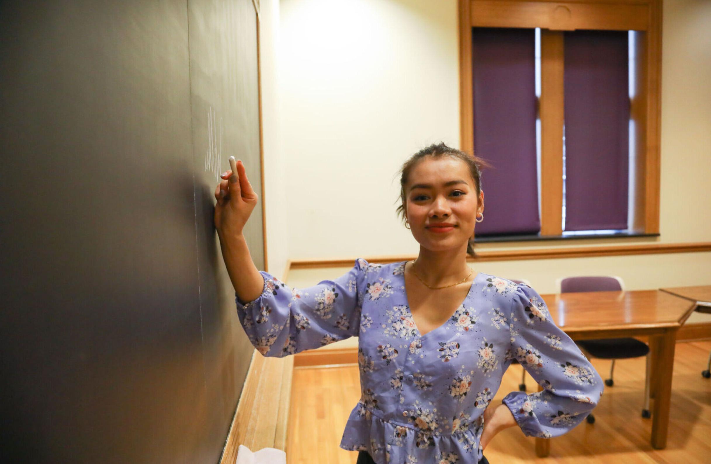 An international student poses as she's writing on a chalkboard